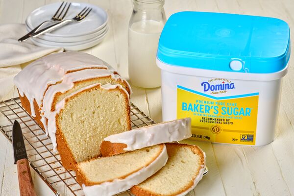A sliced pound cake on a kitchen counter next to a tub of Domino® Baker’s Sugar